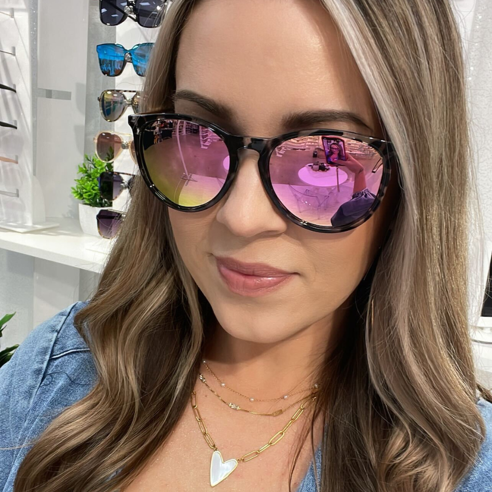 Woman wearing pink-tinted sunglasses with a store interior in the background