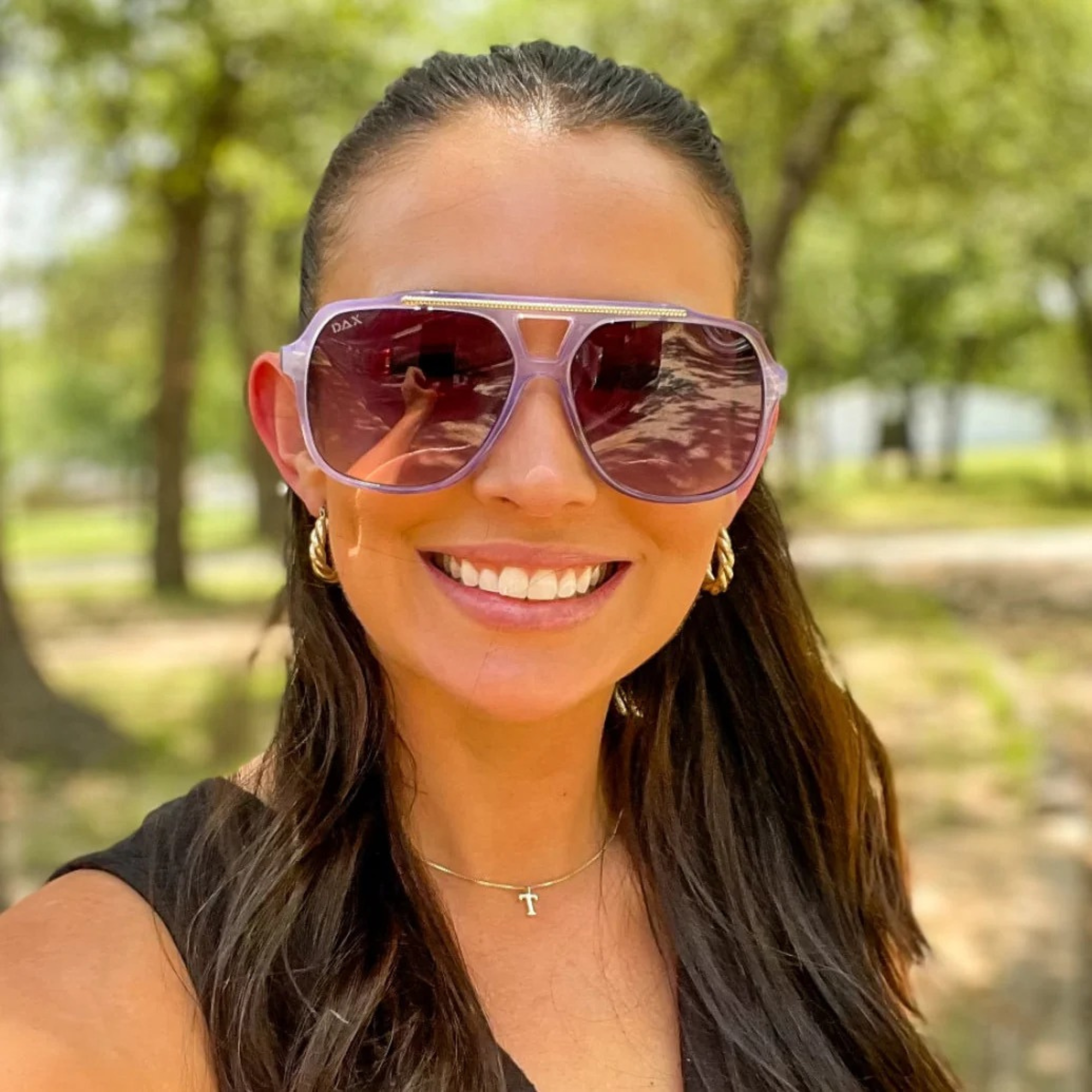 Woman wearing purple sunglasses with a blurred green outdoor background
