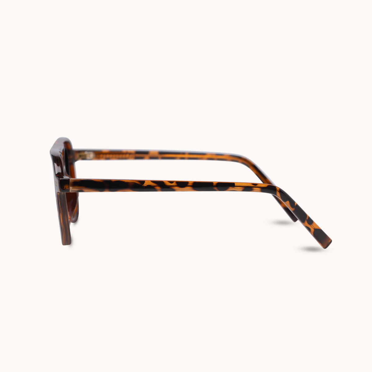A pair of square-frame eyeglasses with a classic tortoiseshell pattern in brown and amber, shown from a side profile view against a light cream background.