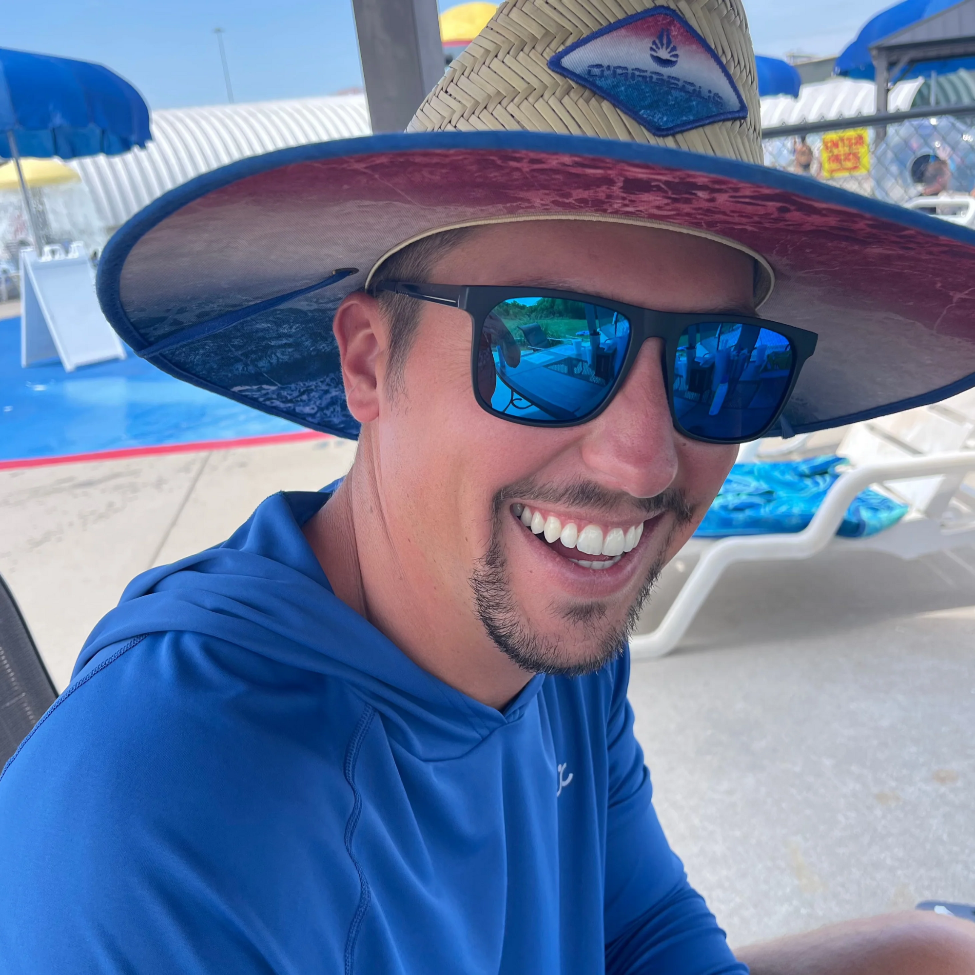 Man wearing a large straw hat and sunglasses with a pool area in the background
