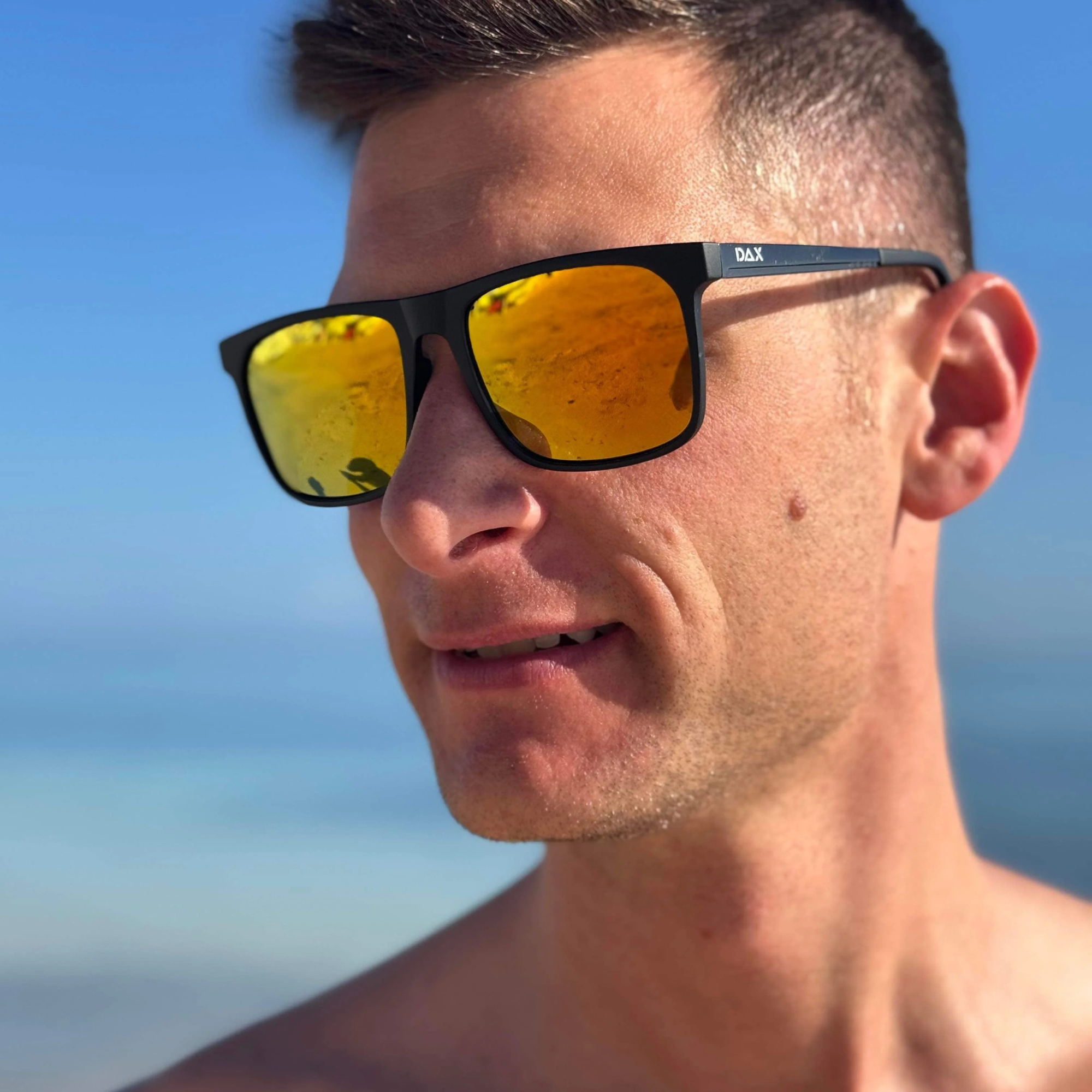 Man wearing sunglasses with a reflective yellow lens against a clear blue sky.