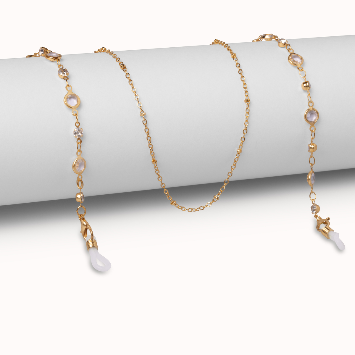 A delicate gold chain necklace draped over a white cylindrical display stand, featuring small gold beads, clear faceted stones, and white teardrop-shaped pendant drops.