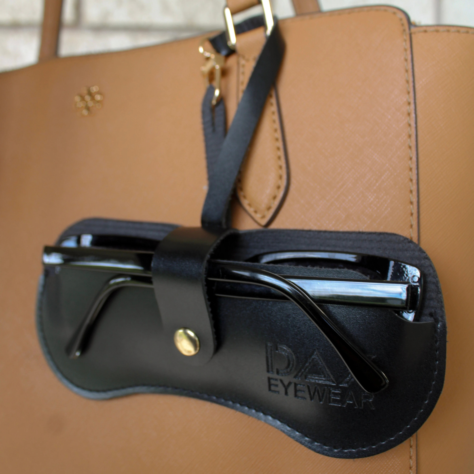 Black eyewear case with 'DAX EYEWEAR' branding on a brown leather handbag.