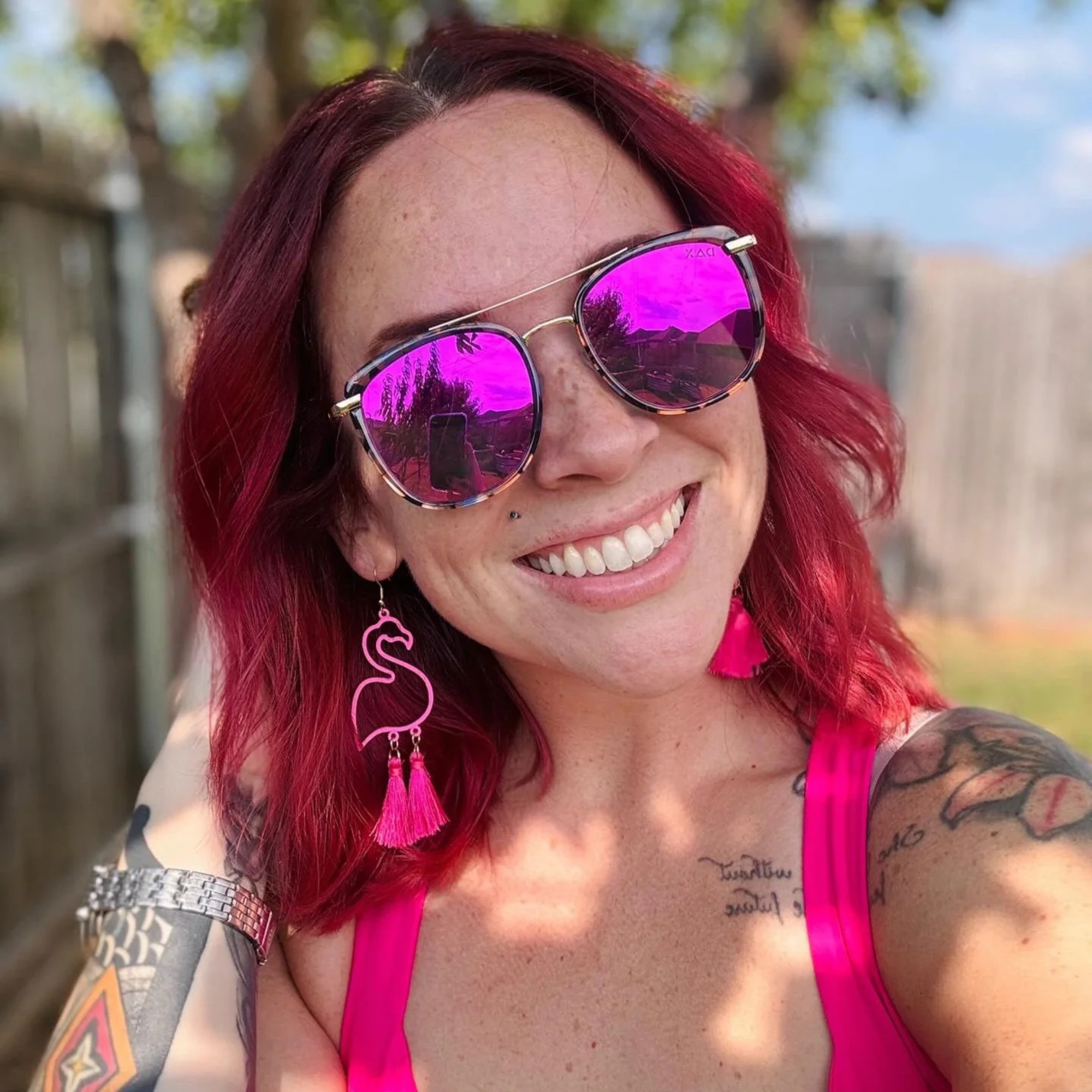 Person with pink hair and sunglasses, wearing a pink top outdoors.