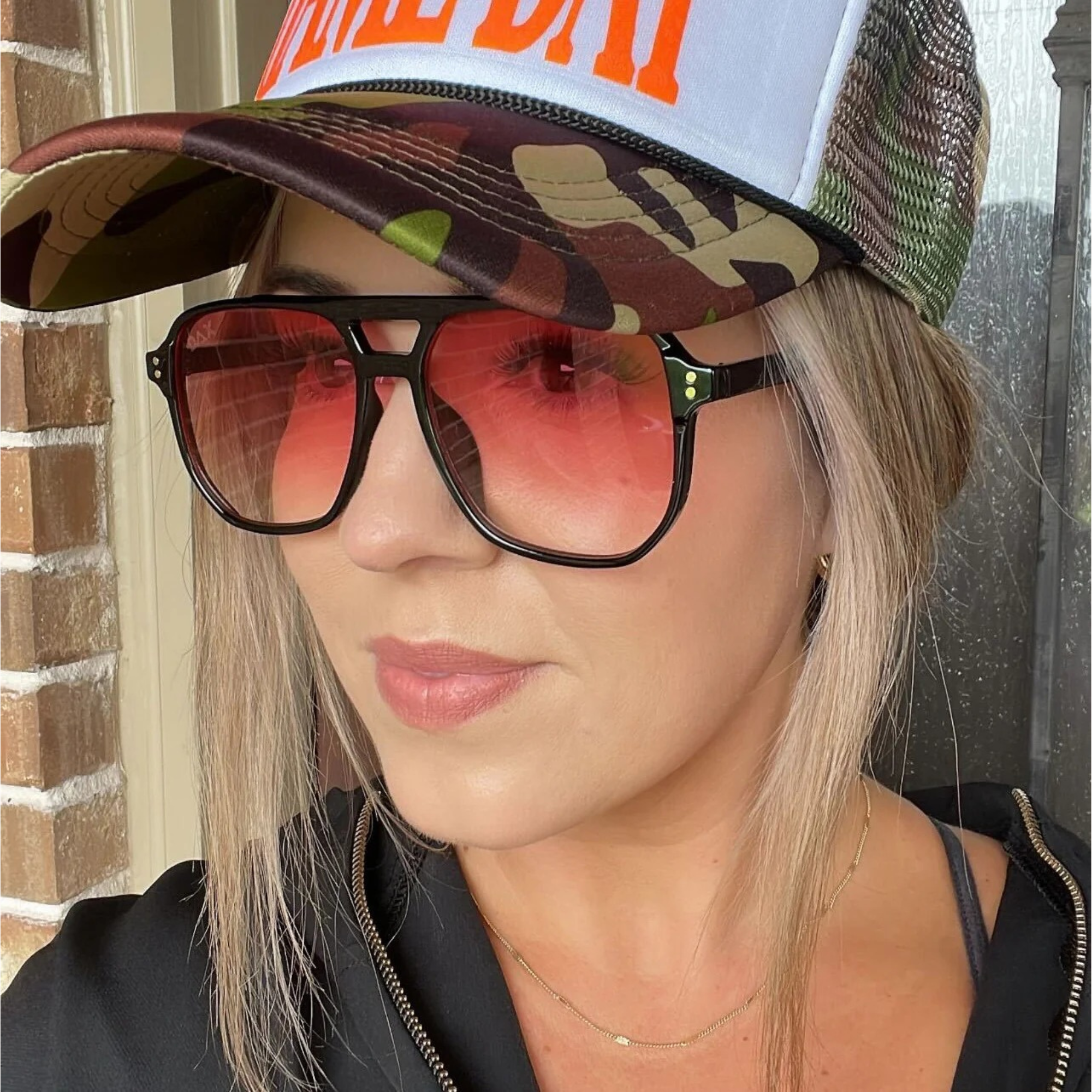 Person wearing a camouflage cap and sunglasses with a neutral background