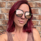 Person with red hair wearing sunglasses in front of a brick wall