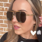 Woman wearing gold sunglasses and heart-shaped earrings against a brick wall.