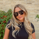 Woman wearing sunglasses with a brick wall and plants in the background