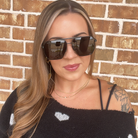 Woman wearing sunglasses and a black top with white patterns against a brick wall.