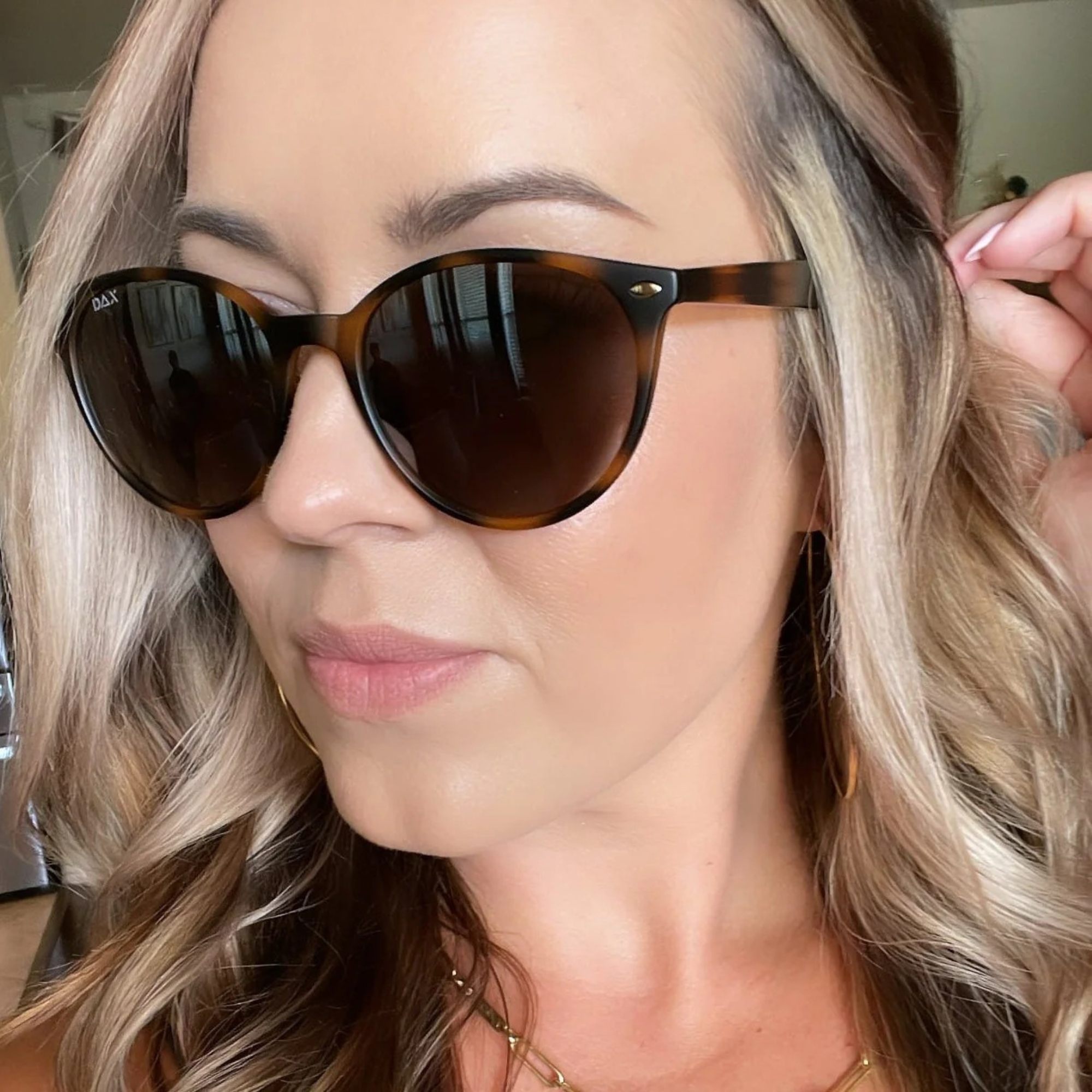 Close-up of a person wearing tortoiseshell sunglasses with a blurred background