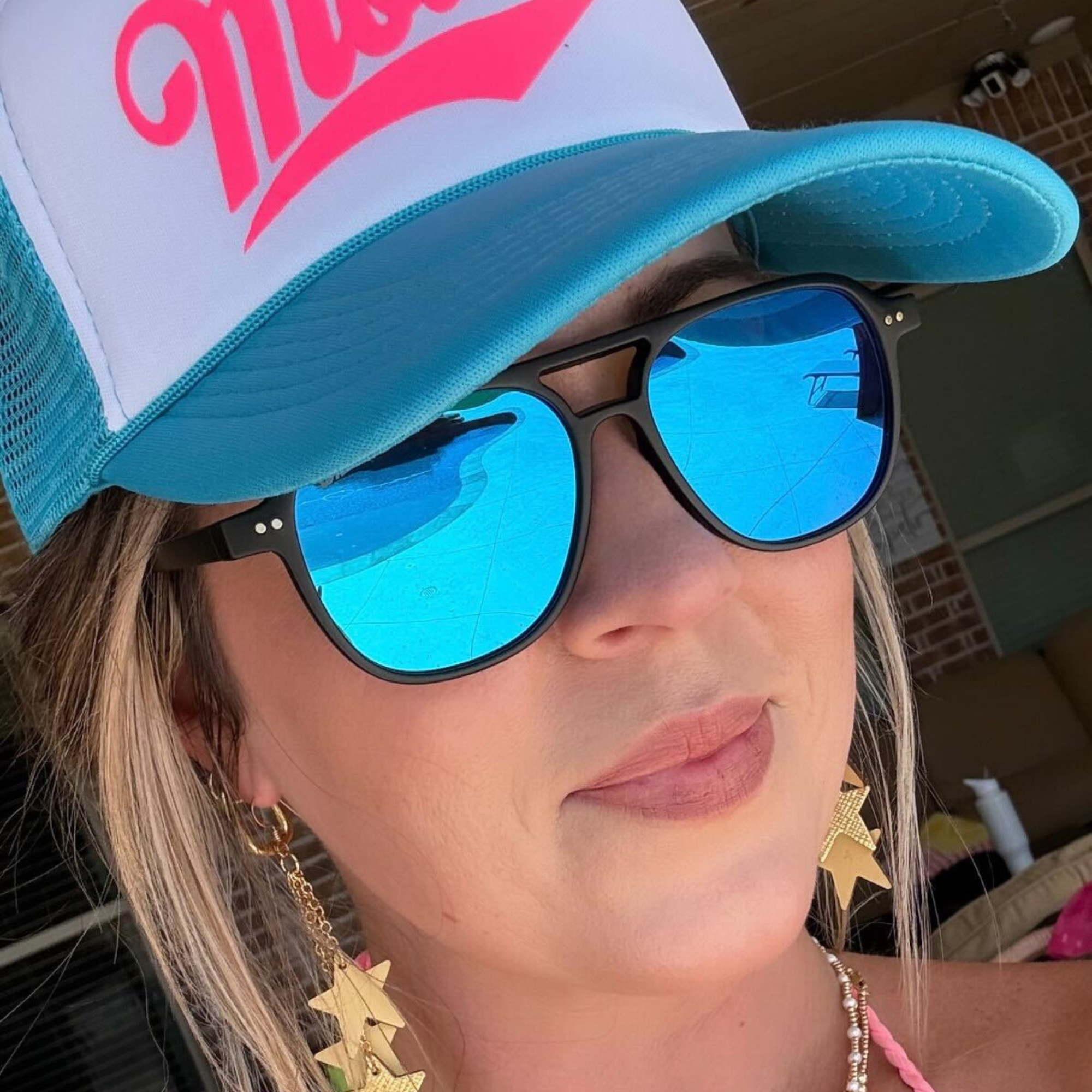 Person wearing a blue and white cap with pink text and reflective sunglasses.