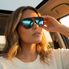 Woman wearing sunglasses inside a car with a scenic reflection.