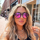 Woman wearing pink reflective sunglasses on a street with brick buildings.