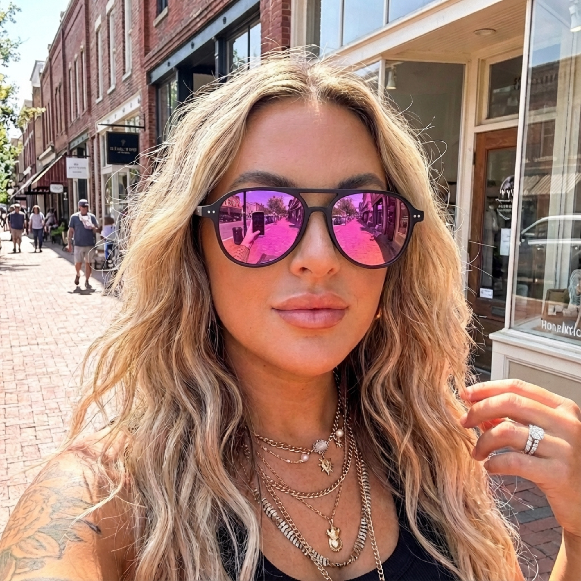 Woman wearing pink reflective sunglasses on a street with brick buildings.