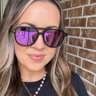 Woman wearing purple reflective sunglasses in front of a brick wall
