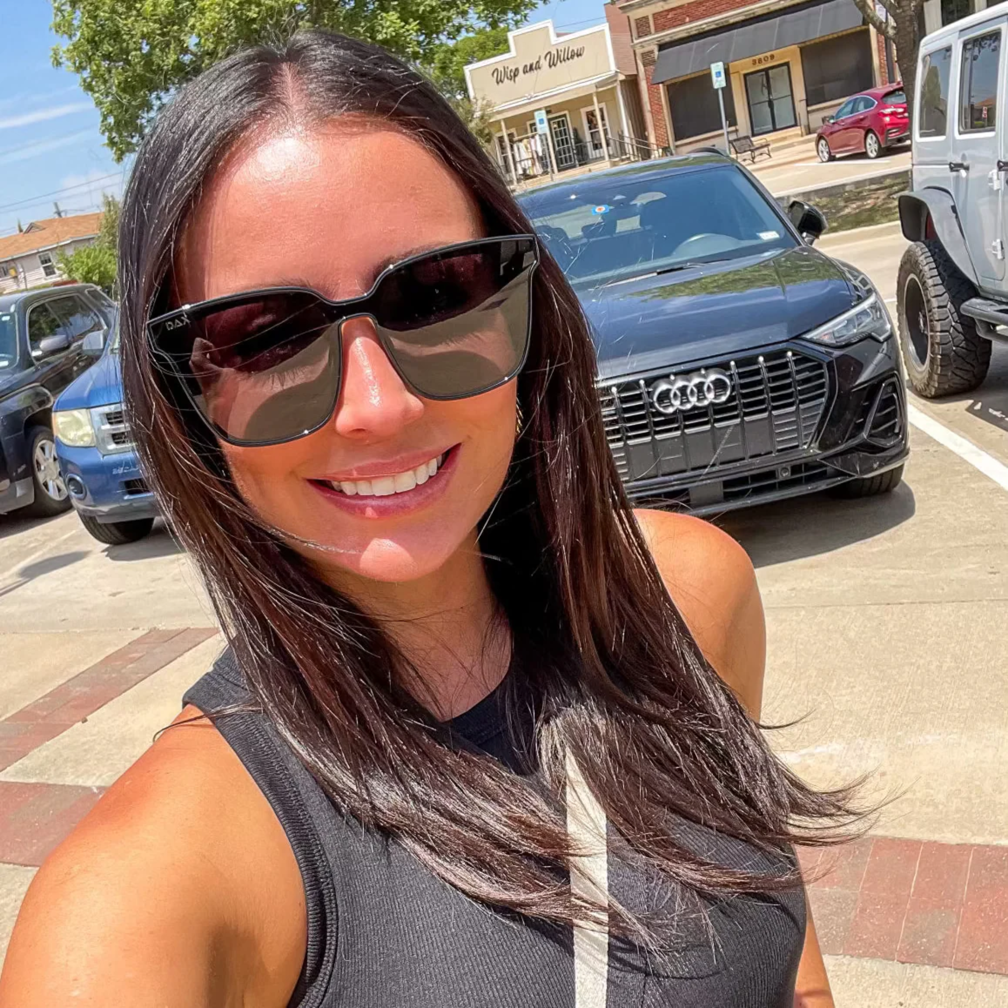 Woman wearing sunglasses with cars and a building in the background