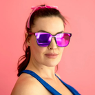 Woman wearing purple sunglasses and a pink headband against a pink background