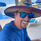 Man wearing a large straw hat and sunglasses with a pool area in the background