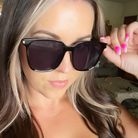 Woman holding up a pair of dark sunglasses with a blurred indoor background