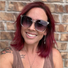 Woman with red hair wearing sunglasses in front of a brick wall