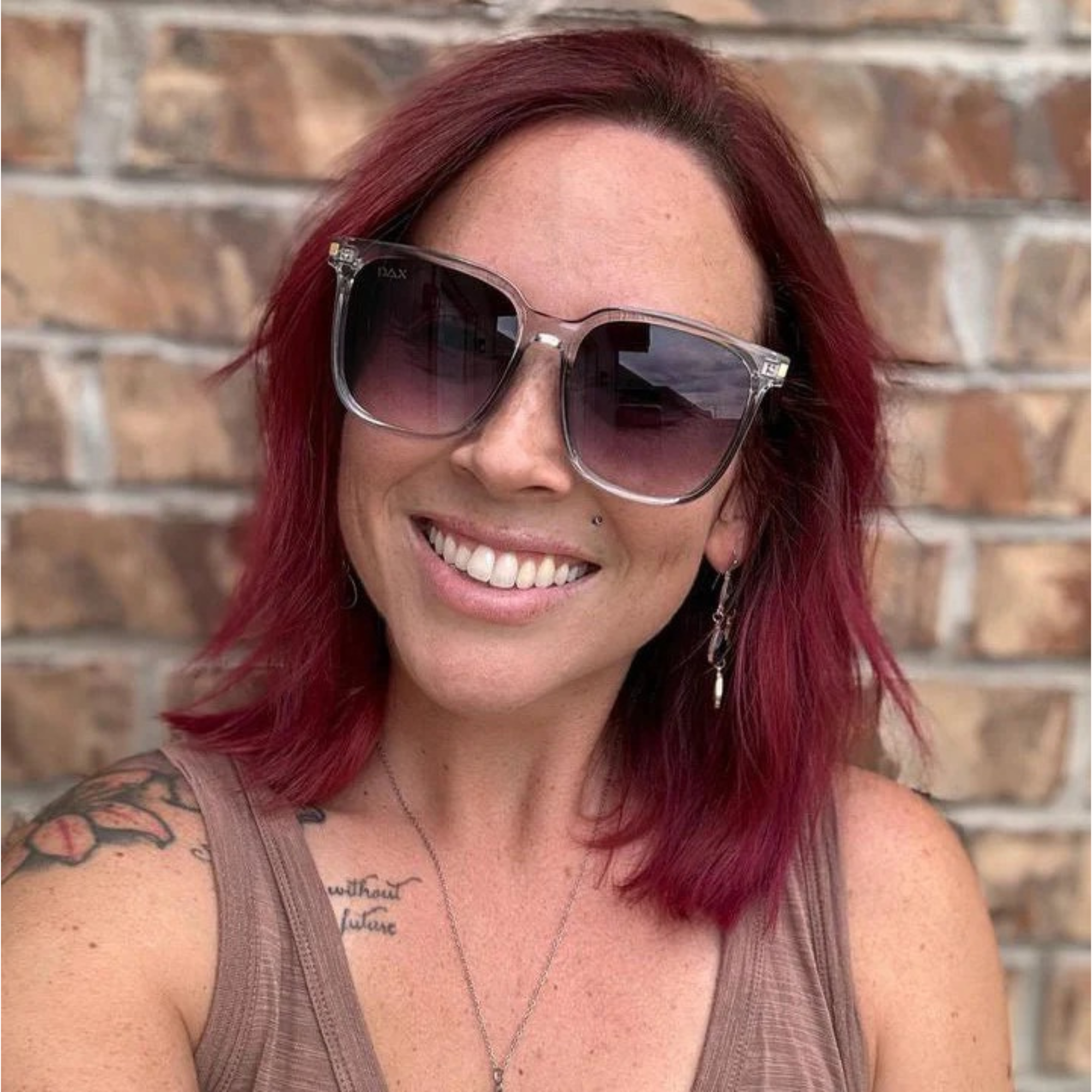 Woman with red hair wearing sunglasses in front of a brick wall