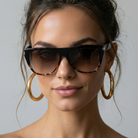 Woman wearing sunglasses and gold hoop earrings against a neutral background