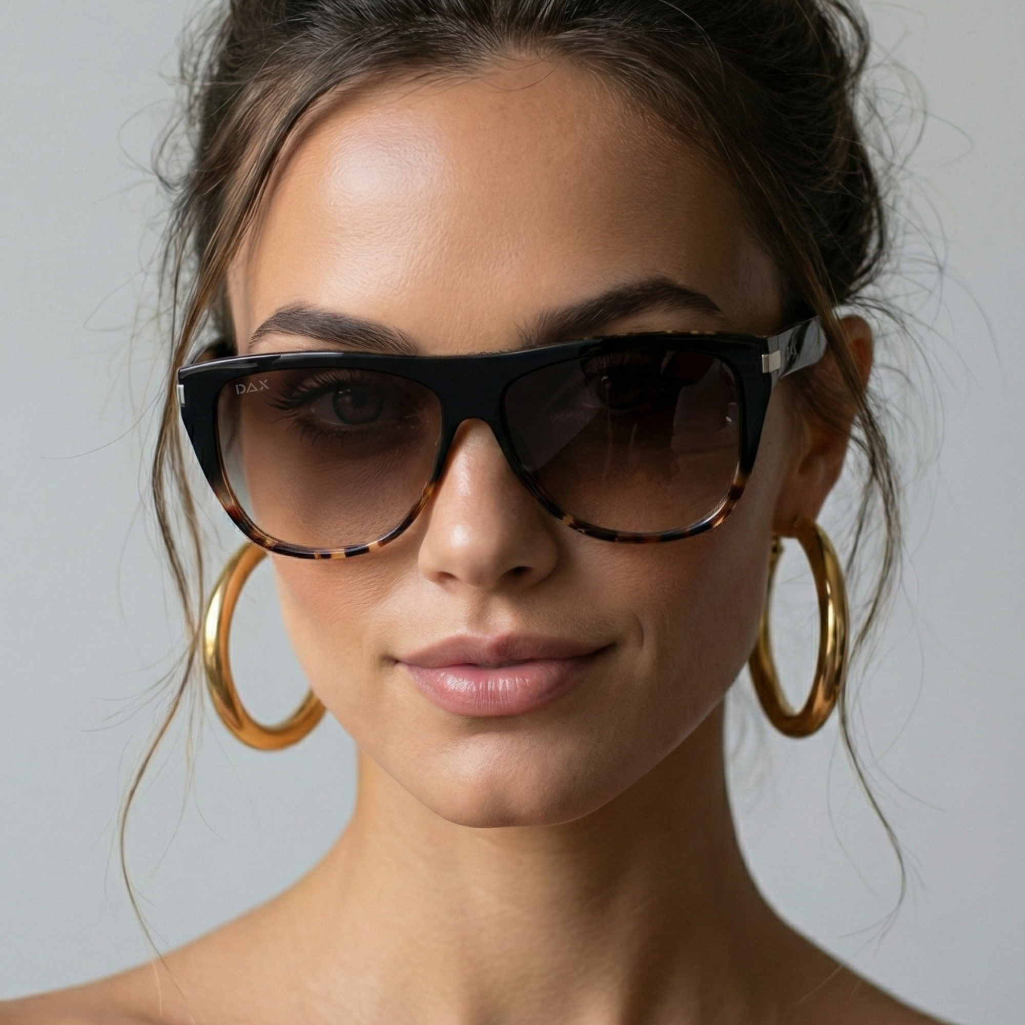 Woman wearing sunglasses and gold hoop earrings against a neutral background