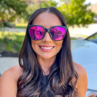 Woman wearing pink reflective sunglasses with a blurred outdoor background