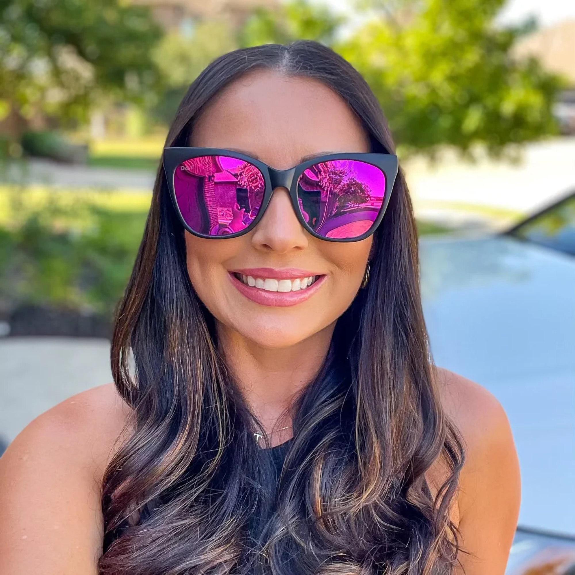 Woman wearing pink reflective sunglasses with a blurred outdoor background