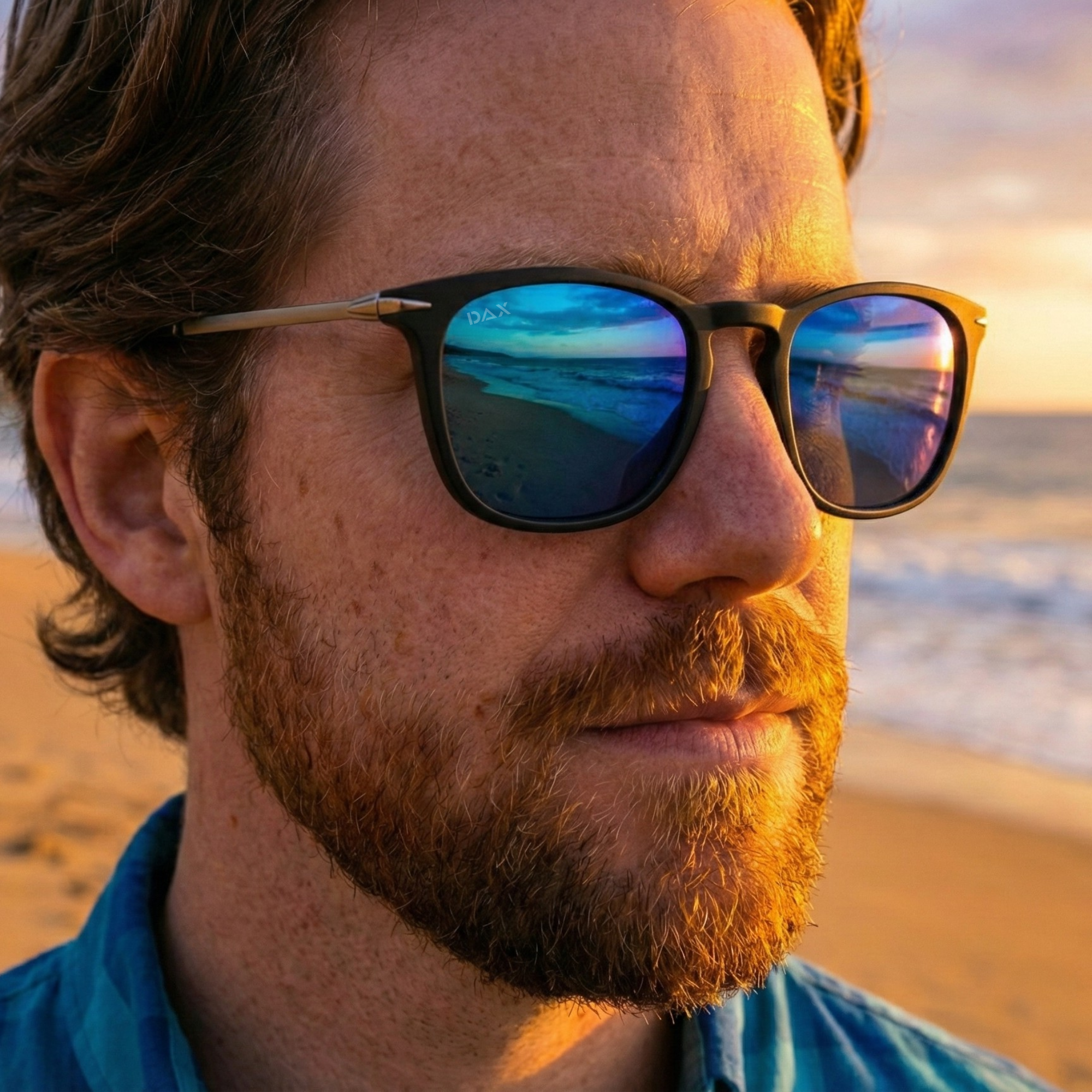 Man wearing sunglasses with a beach reflection, standing on a beach at sunset.