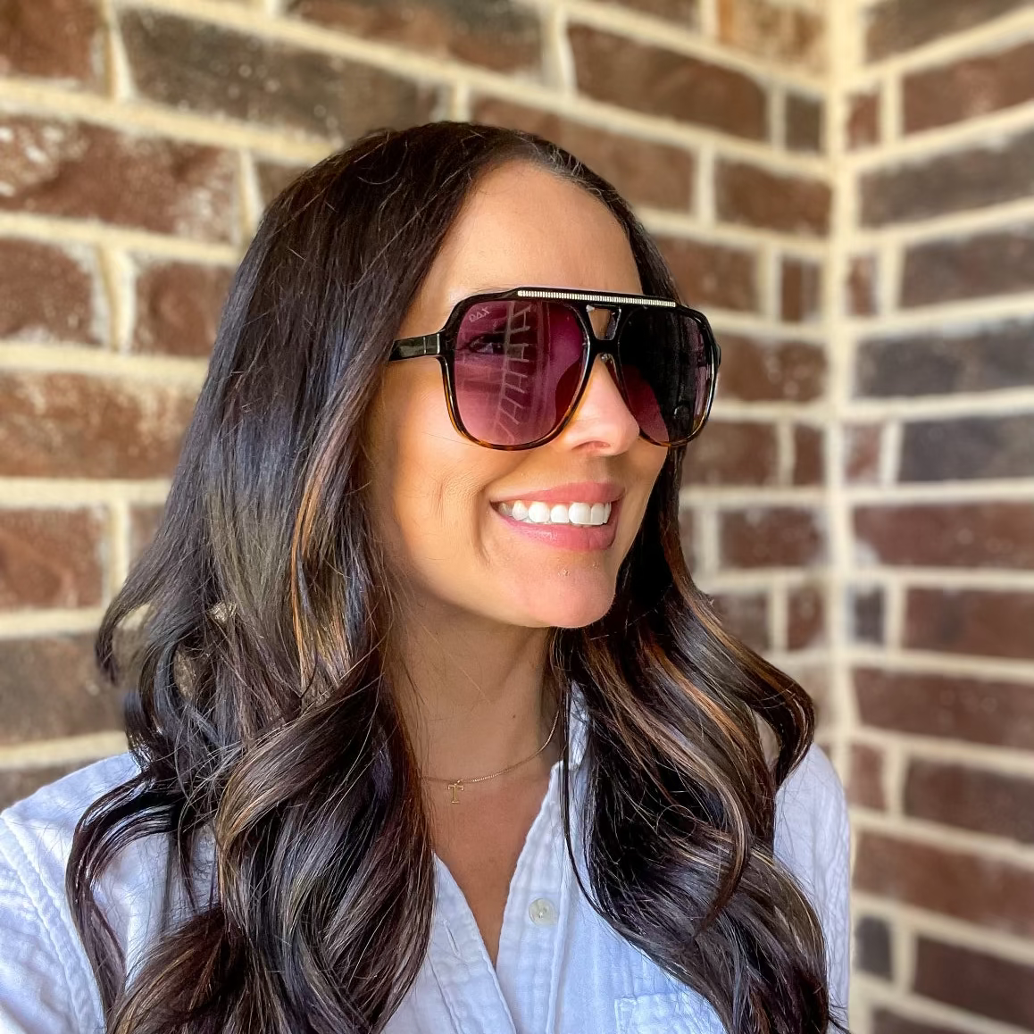 Woman wearing sunglasses and a white shirt against a brick wall