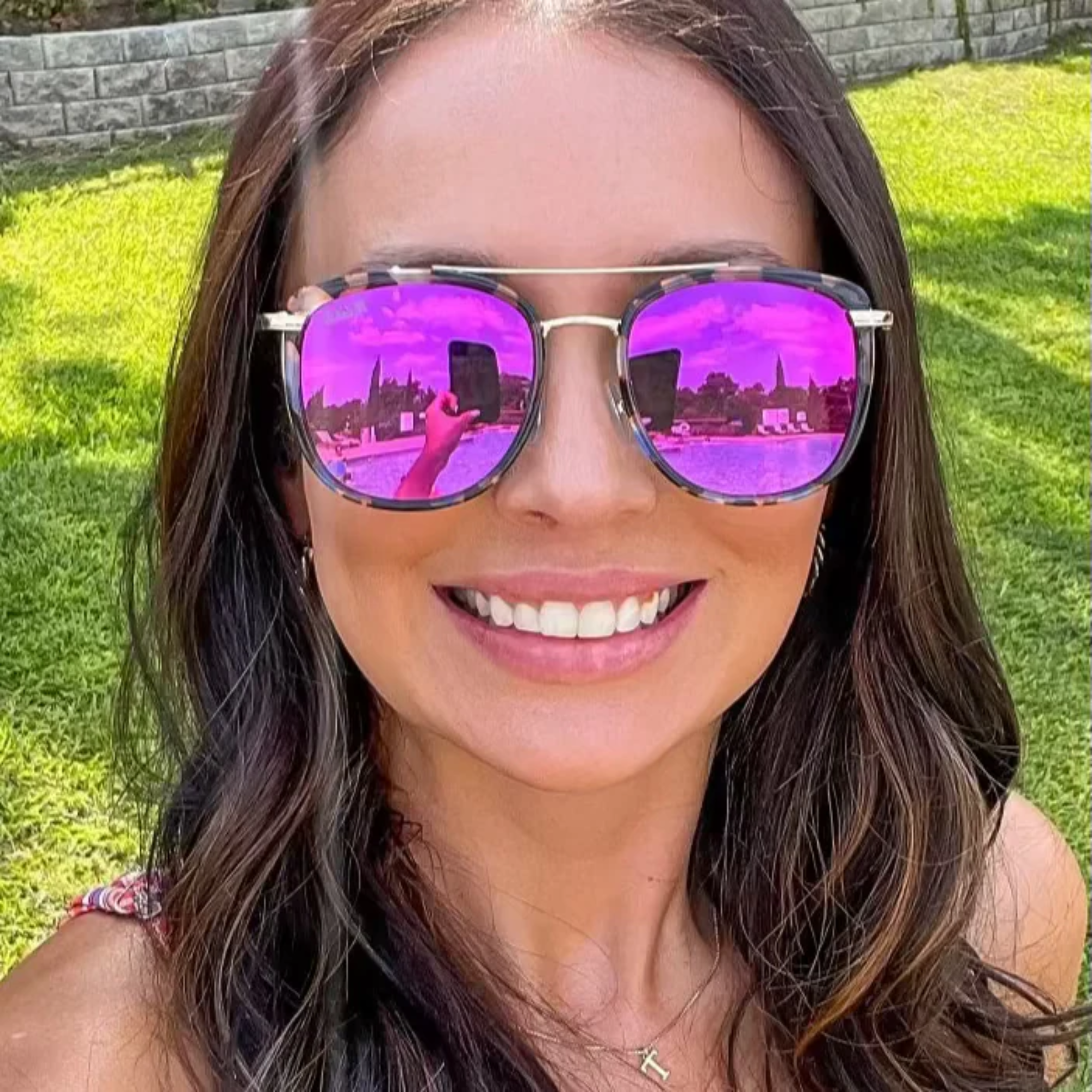 Woman wearing purple reflective sunglasses with a grassy background