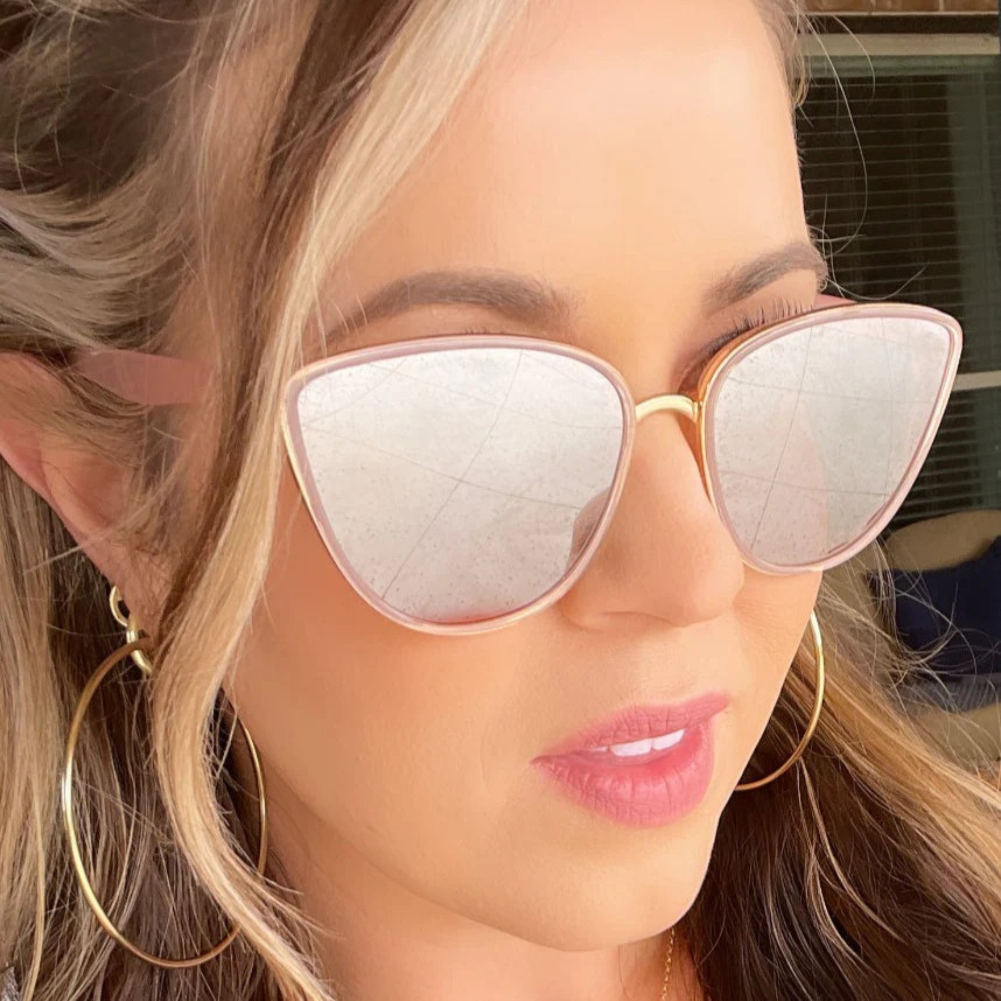 Close-up of a person wearing cat-eye sunglasses with gold frames and reflective lenses.