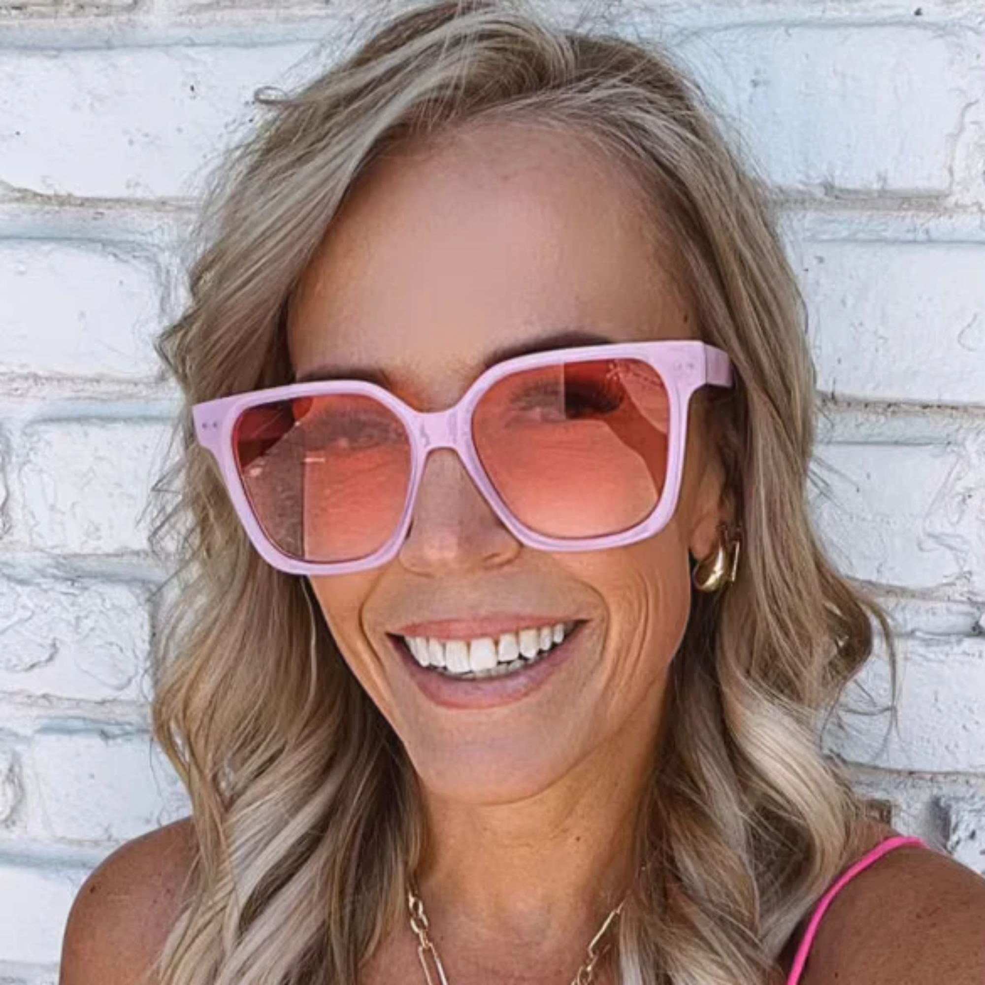 Woman wearing pink sunglasses with a white brick wall background