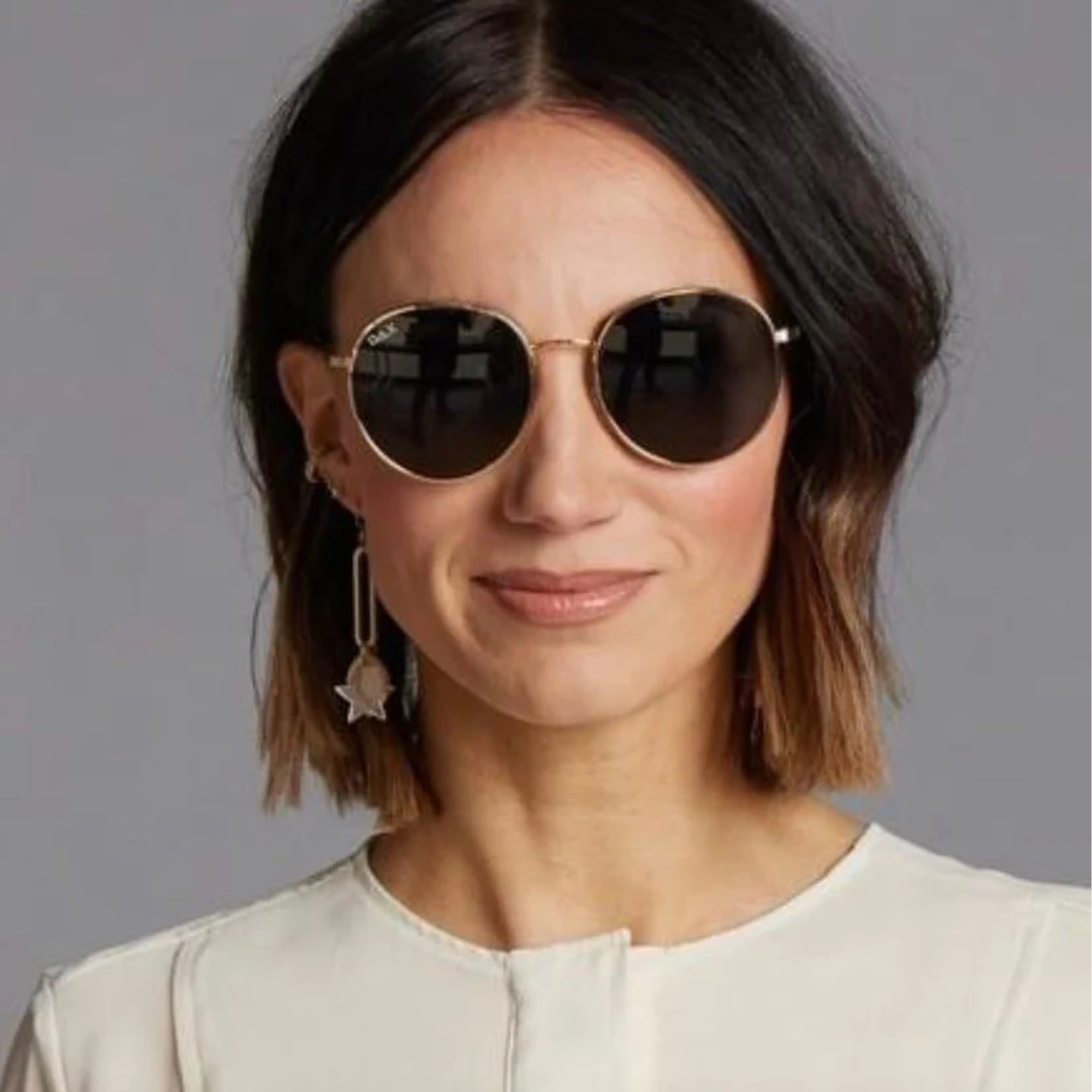 Woman wearing round sunglasses with a neutral background