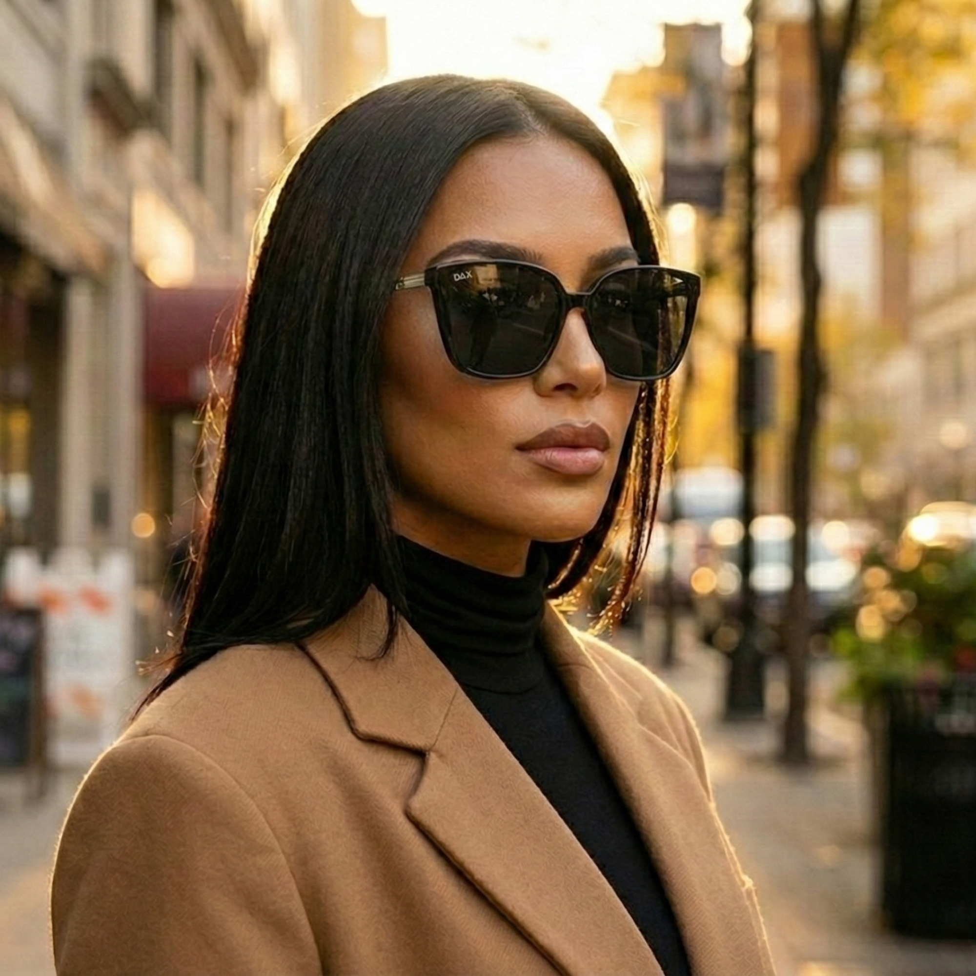 Woman wearing sunglasses and a tan coat on a city street