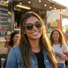 Woman wearing sunglasses smiling in front of a taco truck with friends.