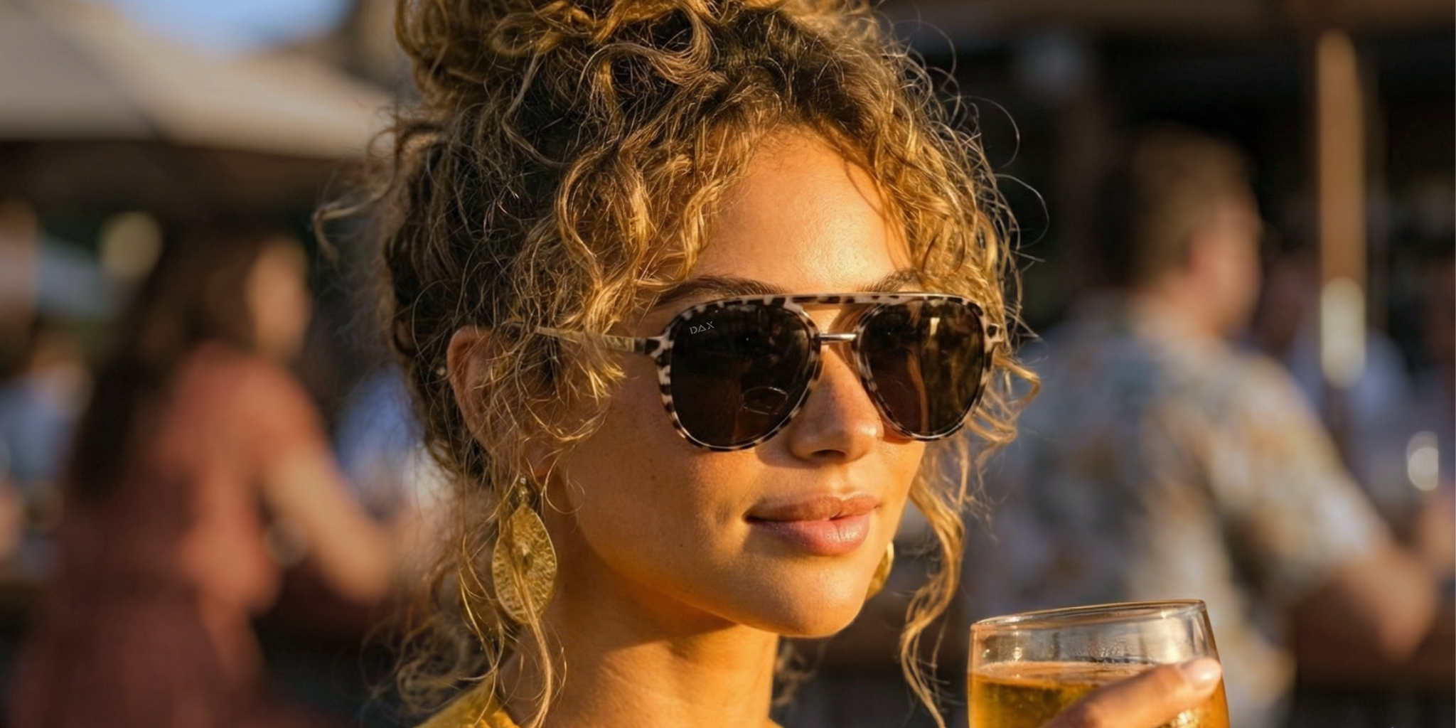 Woman wearing sunglasses and holding a drink in a social setting
