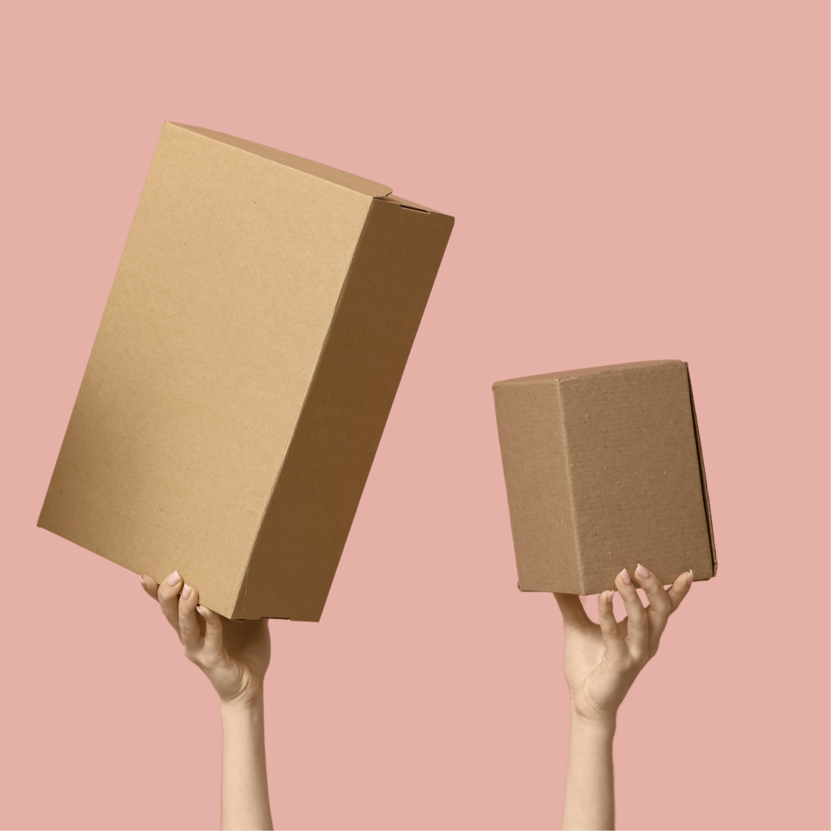 Two plain brown cardboard boxes held up by hands against a solid dusty pink background.
