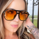 Woman wearing orange-tinted sunglasses with a blurred outdoor background