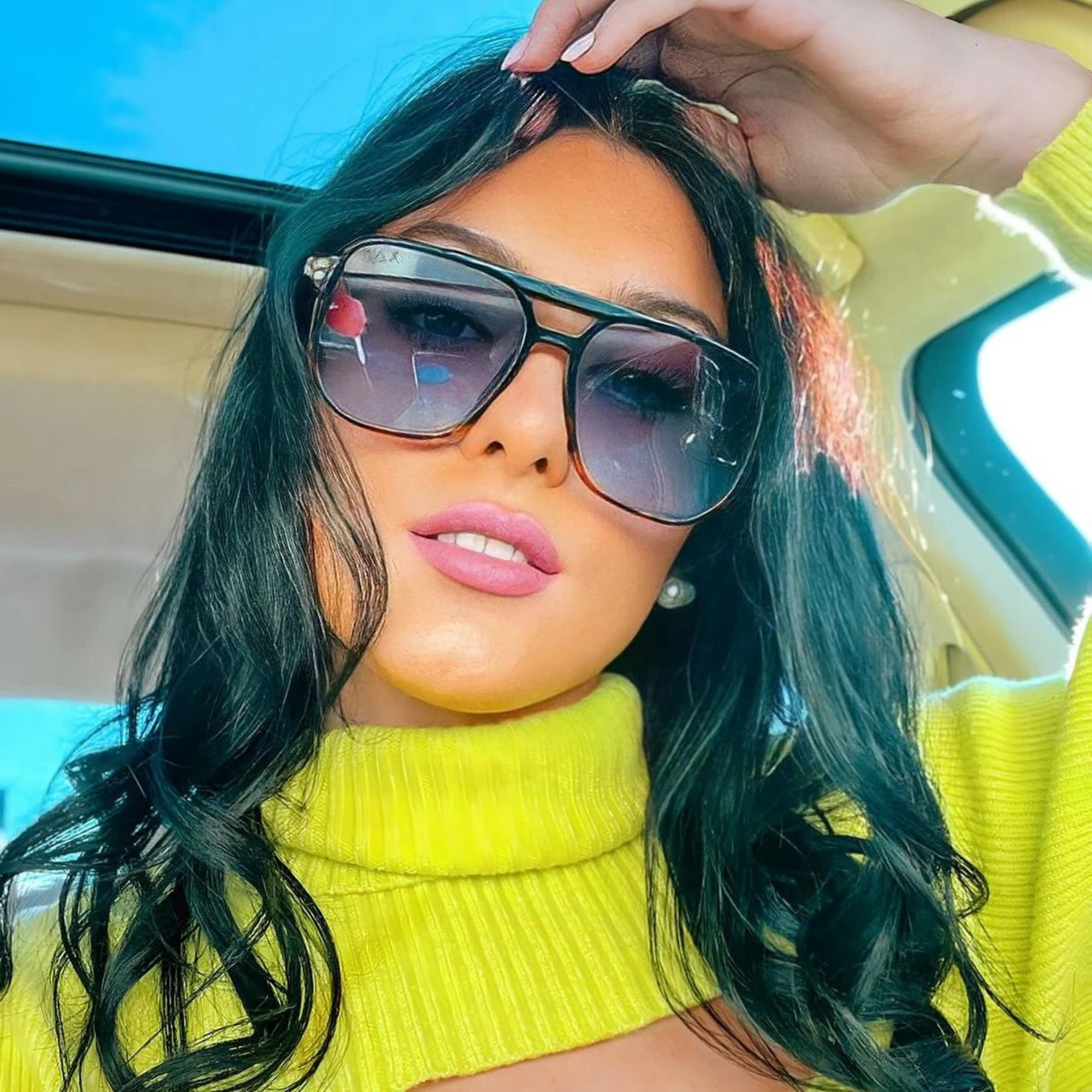 Woman wearing sunglasses and a yellow top inside a vehicle