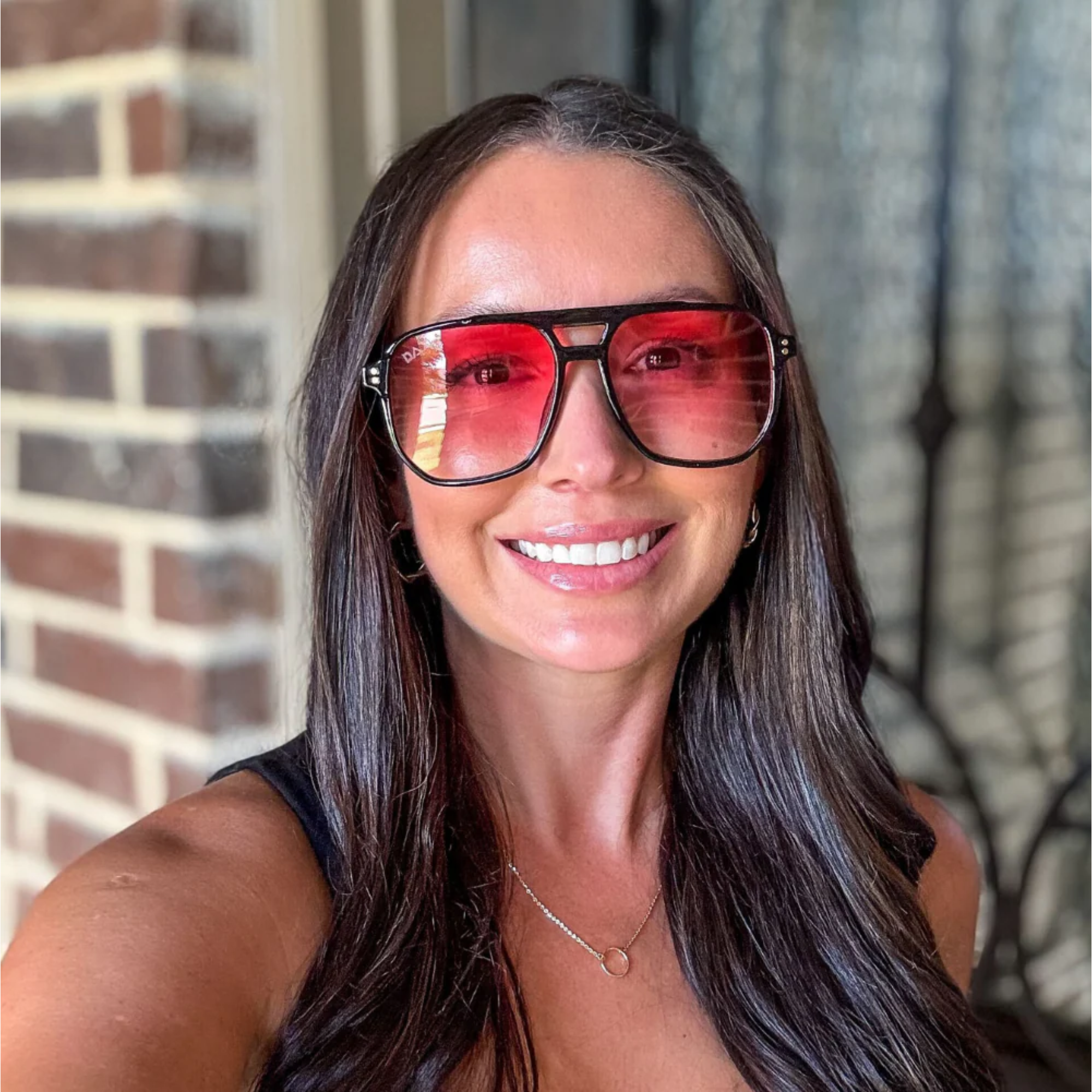 Woman wearing large sunglasses with a brick wall background