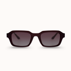A pair of square sunglasses with a translucent dark burgundy frame and gradient gray lenses, shown against a plain off-white background.